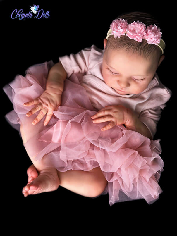 Reborn Laura is sleeping while dressed in a pink tutu and matching flower head band.